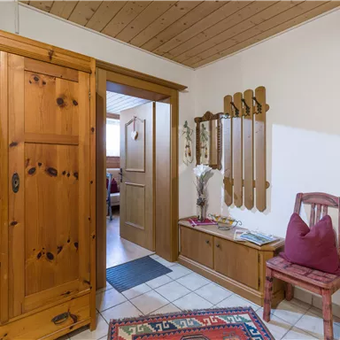 A cozy hallway with wooden cabinets and a seating area. The walls are light and the floor is tiled.