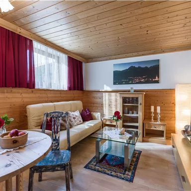 A cozy living space with wooden paneling, a comfortable sofa, and a table. The windows let in plenty of light, and there are decorative elements like flowers and artworks.