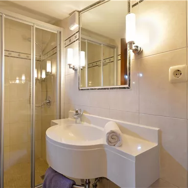 A modern bathroom with a shower and an oval sink. The walls are brightly tiled and a large mirror reflects the light.