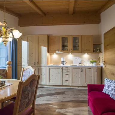 A cozy kitchen with wood paneling and modern appliances. The dining area has a round table and a red armchair.