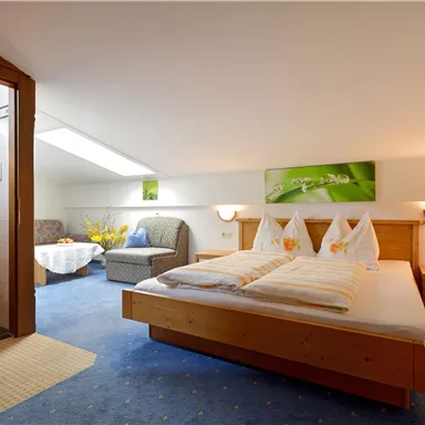 A cozy hotel room with two beds and a large window. In the background, a bathroom and a comfortable seating area can be seen.