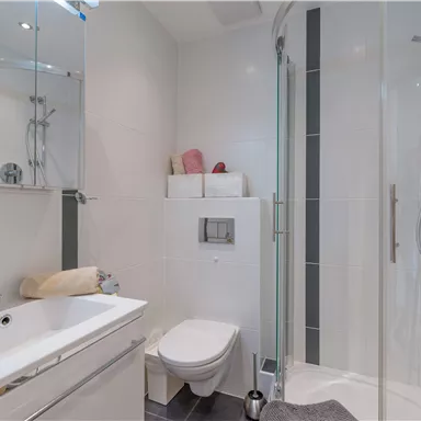 Ein modernes Badezimmer mit einer Dusche, einem Waschbecken und einer Toilette. Die Wände sind hell und die Ausstattung ist zeitgemäß.