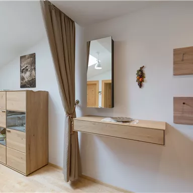 Ein moderner Wohnbereich mit Holzregalen und einem Spiegel. Der Raum ist hell und freundlich, mit einer gemütlichen Atmosphäre.