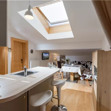 Eine moderne Küche mit einem großen Fenster und Holzoberflächen. Der Raum ist hell und einladend, mit einem Tisch für die Mahlzeiten.