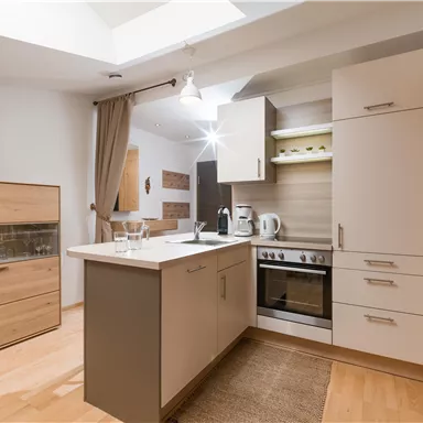 Eine moderne Küche mit hellen Holzoberflächen und einem großen Fenster. Es gibt einen Herd, eine Spüle und ausreichend Stauraum.