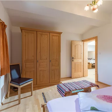 Ein helles Schlafzimmer mit einem Holzschrank und einem Stuhl. Die Einrichtung ist einfach und gemütlich.