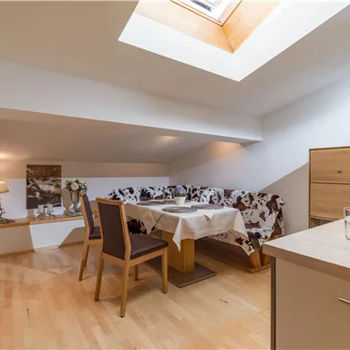 Ein gemütlicher Wohnbereich mit einem Esstisch und einer Couch. Das Zimmer hat ein Dachfenster und helles Holzfußboden.