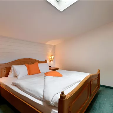 A cozy bedroom with a large bed and wooden details. There are bedside lamps and a small desk.