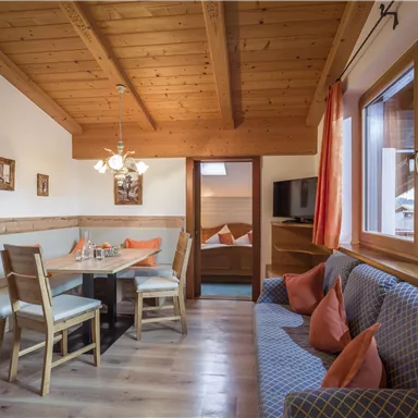 A cozy living space with a wooden beam ceiling. There is a dining area with chairs and a couch with pillows.