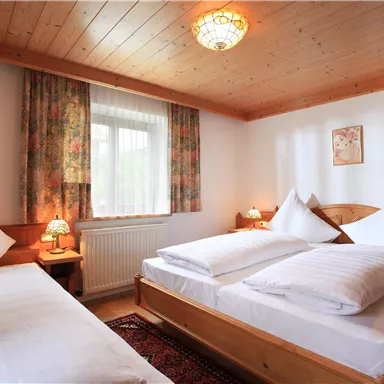 Ein gemütliches Schlafzimmer mit zwei Betten und einer warmen Holzdecke. Helle Fenster und ein Teppich verleihen der Atmosphäre eine einladende Note.