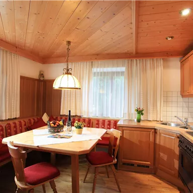 Eine gemütliche Küche mit Holzdecken und einem runden Tisch. Rote Polsterstühle und eine Kochzeile schaffen eine einladende Atmosphäre.