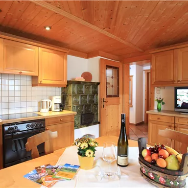 Eine gemütliche Küche mit Holzschränken und einem Tisch mit Obstkorb. Ein Fernseher und eine angenehme Atmosphäre sorgen für ein einladendes Ambiente.