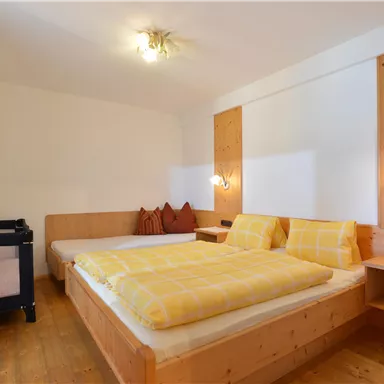 Ein gemütliches Zimmer mit zwei Betten in Holzoptik und gelben Bettdecken. Es gibt auch einen Wickeltisch in der Ecke und sanfte Beleuchtung.