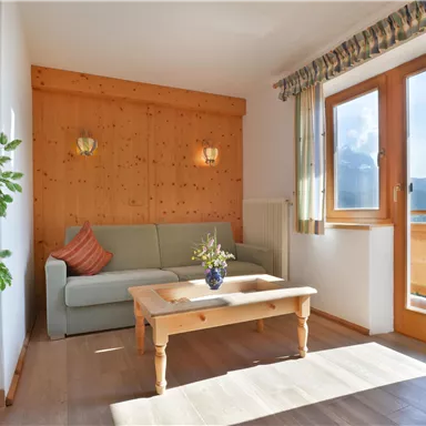 Ein heller Wohnraum mit einer gemütlichen Couch und einem Tisch. Große Fenster bieten einen Blick auf die Natur.