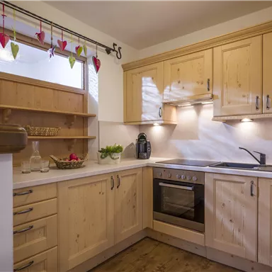 A modern kitchen with wooden furniture and a bright, inviting atmosphere. It is well-equipped with a stove, sink, and windows that let in plenty of light.