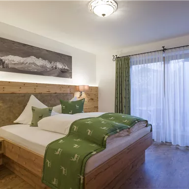 A modern bedroom with a large double bed and wooden paneling. Large windows allow plenty of daylight in and provide a view outside.