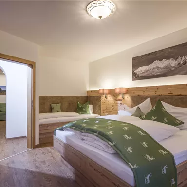 A cozy bedroom with wooden details and two beds. The walls are light and there is a large window that lets in natural light.