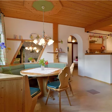 A cozy kitchen with wooden ceilings and a dining area. The room is bright and inviting, with plants on the table and functional kitchen elements.