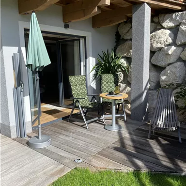 A cozy terrace with two chairs and a small table. A sunshade and green spaces create a relaxed atmosphere.