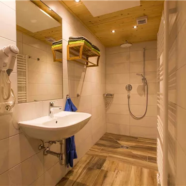 Ein modernes Badezimmer mit einer Dusche und einem Waschbecken. Die Wände sind gefliest und es gibt Holzverkleidungen an der Decke.