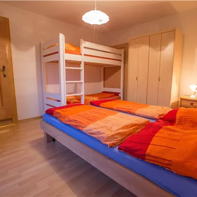 Ein gemütliches Schlafzimmer mit einem Stockbett und zwei Einzelbetten. Der Raum hat einen warmen Holzton und ist gut beleuchtet.