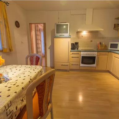 Eine helle und freundliche Küche mit Holzschränken und modernen Geräten. Am Tisch steht eine kleine Blumendekoration.