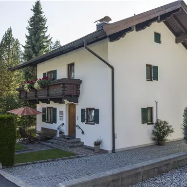 Ein schönes Haus mit einem Balkon und grünen Fensterläden. Umgeben von Bäumen und einem gepflegten Garten.