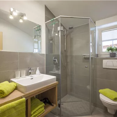 Ein modernes Badezimmer mit einer Glasdusche und einem Waschbecken. Handtücher in frischem Grün sorgen für einen farbenfrohen Akzent.