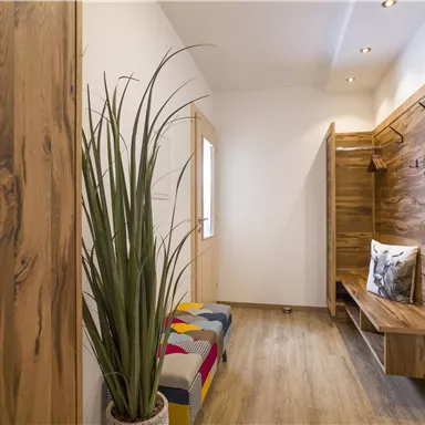 Ein moderner Eingangsbereich mit Holzverkleidungen. Eine Pflanze und eine farbenfrohe Bank sorgen für eine gemütliche Atmosphäre.
