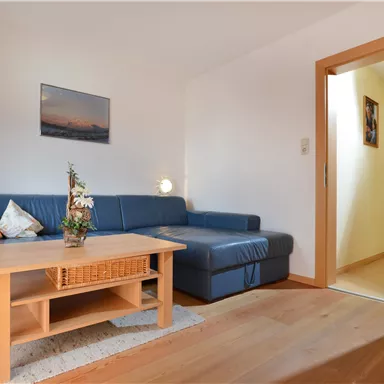 Eine gemütliche Wohnung mit einem blauen Sofa und einem Holztisch. Der Raum wirkt hell und einladend.