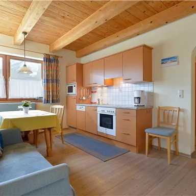 Eine gemütliche Küche mit einem Esstisch und modernen Geräten. Holzdecken und eine warme Atmosphäre schaffen ein einladendes Ambiente.