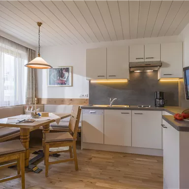 A modern kitchen with a table and chairs. The decor is bright and inviting, with wooden flooring and a television.