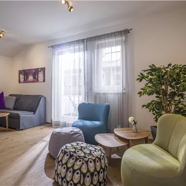 Ein modernes Wohnzimmer mit bequemen Möbeln und großen Fenstern. Es gibt einen pflanzenartigen Akzent und stilvolle Tischchen.