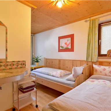 A cozy room with two single beds and wooden paneling. A small washing area and a window provide brightness and an inviting atmosphere.