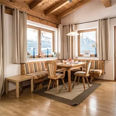 Ein gemütlicher Essbereich mit Holztisch und Stühlen. Große Fenster bieten einen Blick auf die Berge und viel Tageslicht.