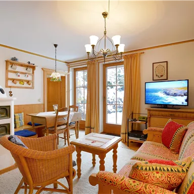 A cozy living room with a sofa, a table, and a television. The room design is warm and inviting, with a wood stove and plenty of natural light.