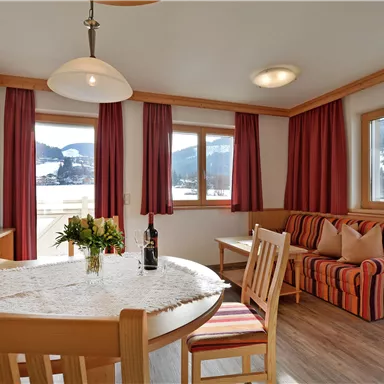 A cozy living room with a dining table and a sofa. Large windows offer a view of the mountains.