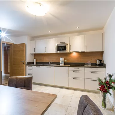 Eine moderne Küche mit hellen Schränken und einer neutralen Farbpalette. Der Raum ist gut beleuchtet und hat einen Esstisch mit gemütlichen Stühlen.