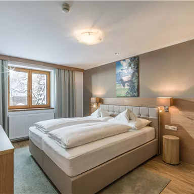 Ein modernes Schlafzimmer mit einem großen Bett, Holzmöbeln und einem Fenster mit Vorhängen. An der Wand hängt ein Bild, das dem Raum eine gemütliche Atmosphäre verleiht.