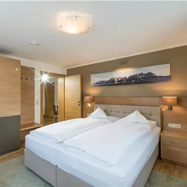 Ein modernes Schlafzimmer mit einem großen Doppelbett und hellen Holzverkleidungen. Die Wände sind in sanften Farben gestrichen, und ein Bild von Bergen hängt über dem Bett.