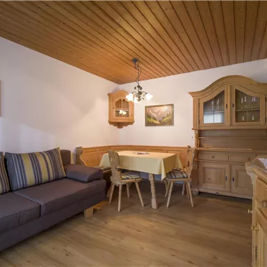 Ein gemütlicher Wohnraum mit einem grauen Sofa und einem Essbereich. Holzverkleidungen und Möbel verleihen dem Raum eine warme Atmoshäre.