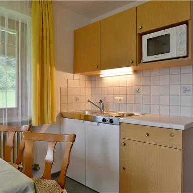 A cozy kitchen with bright cabinets and a microwave oven. The table is set, and there is a view of greenery through the window.