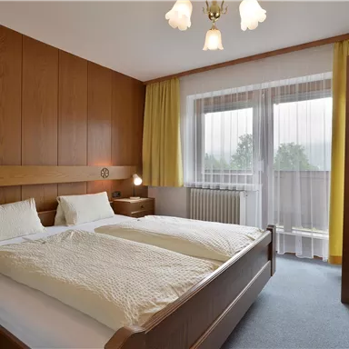 A cozy bedroom with a double bed and two bedside tables. Large windows provide plenty of daylight.