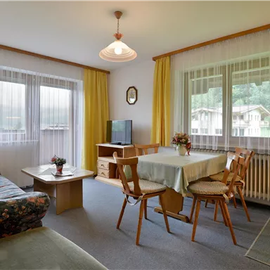 A cozy living space with a sofa, a dining table, and chairs. Large windows provide plenty of daylight and a friendly atmosphere.