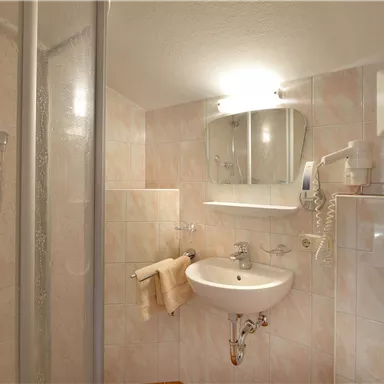 A modern bathroom with a shower and a sink. The walls are decorated with light tiles.