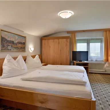 A cozy hotel room with two beds and wooden furniture. The room has a window with plenty of daylight and a TV corner.