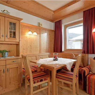 A cozy dining area with wood paneling and a table with chairs. The windows let in plenty of light, and the decoration creates an inviting atmosphere.