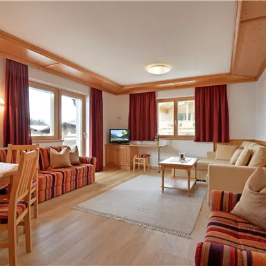 A cozy living room with wooden furnishings and large windows. There are comfortable seating options and a dining table.