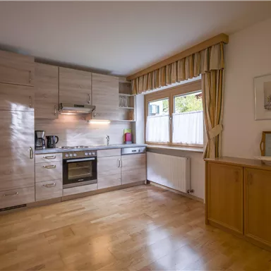 Eine moderne Küche mit Holzschränken und hellen Wänden. Die Küchenausstattung umfasst einen Herd, einen Kühlschrank und ein Fenster mit Vorhängen.