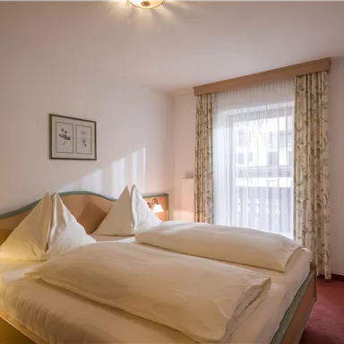 Ein gemütliches Schlafzimmer mit zwei Einzelbetten und eleganter Bettwäsche. Der Raum ist hell und einladend, mit Fenster und Vorhängen, die natürliches Licht hereinlassen.